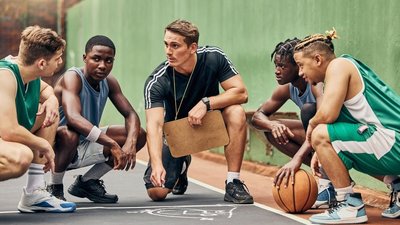 Trainer kniet am Boden und ist im Gespräch mit seinem Basketballteam 