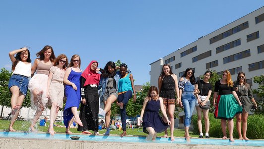 Eine Gruppe an jungen Studentinnen stehen vor einem Pool und lächeln in die Kamera