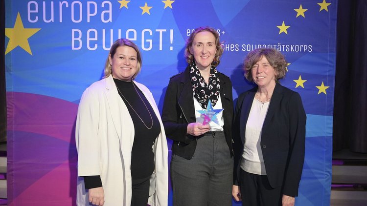 Drei Frauen stehen vor einem Transparent mit der Aufschrift "Europa bewegt" und lachen in die Kamera.