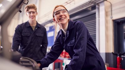 Junge Frau mit Schutzbrille steht neben jungem Mann mit Schutzbrille