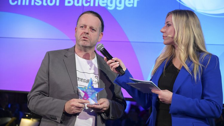 Mann auf Bühne wird von Frau auf Bühne interviewt