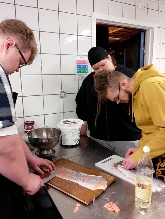 Drei Personen in der Küche bearbeiten Fischfilets