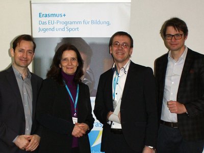 Group photo with 3 men and a woman in front of a roll up with the wording Erasmus+