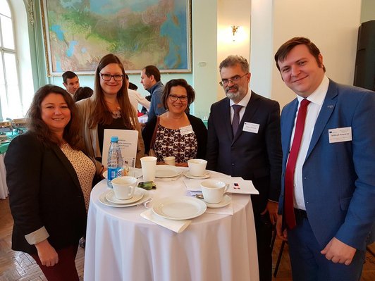 Gruppe von fünf Personen posiert an einem Stehtisch für ein Foto im Veranstaltungssaal