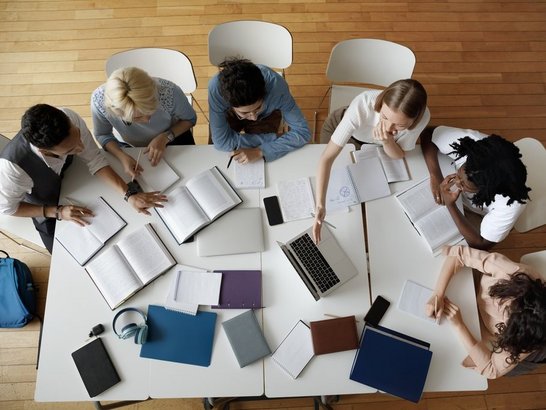 Gruppe von sechs Studierenden sitzt gemeinsam lernend an einem großen Tisch