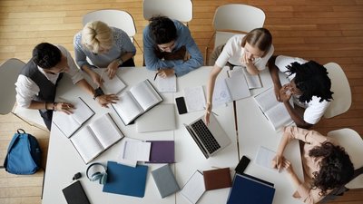 Gruppe von sechs Studierenden sitzt gemeinsam lernend an einem großen Tisch