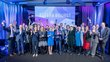 The photo shows all 18 award winners and VIPS at the award ceremony. They stand on a stage and hold their star-shaped trophy in the air.