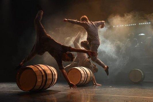  Circus performance: men artfully jump over moving barrels.