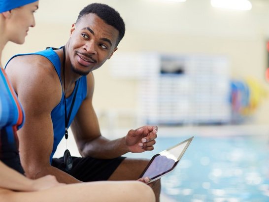 1130365667 Schwimmtrainer im Gespräch mit Athletin in Schwimmhalle