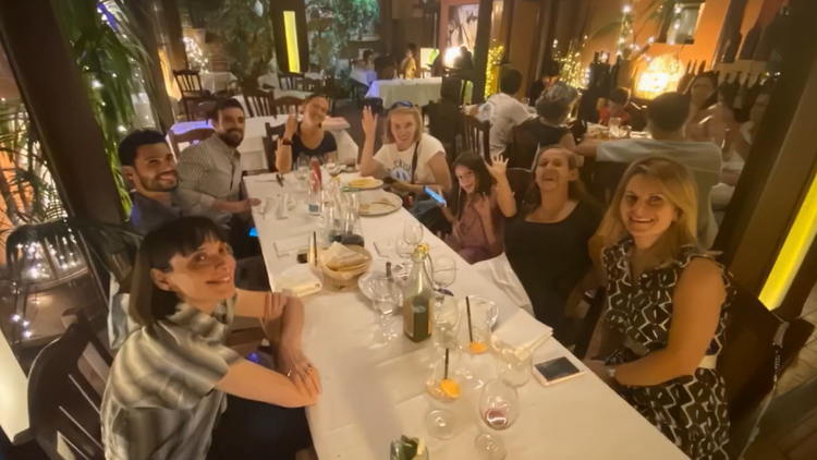 Gruppe an acht Personen sitzt gemeinsam in einem Restaurant an einem Tisch und lacht in die Kamera