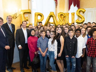 Gruppenfoto von dem österreichischen Bildungsminister und einer Schulkasse in einem Raum. Im Hintergrund sit das Wort Erasmus mit Ballonen geschrieben.