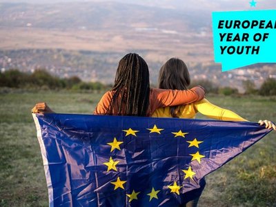 Sujetbild Europäisches Jahr der Jugend 2022: Zwei Frauen stehen mit dem Rücken zur Kamera und schauen auf eine Wiese. Gemeinsam halten sie eine Flagge mit dem EU Emblem.