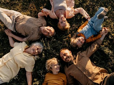 Kinder und Erwachsene liegen im Kreis auf einer Wiese und lachen 