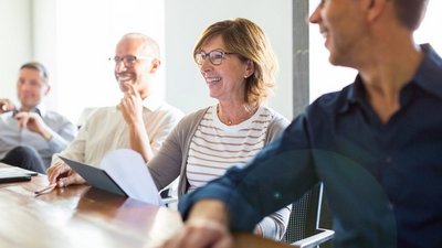 Vier Personen, drei Männer und eine Frau, sitzen gemeinsam an einem Tisch, blicken lachend in eine Richtung