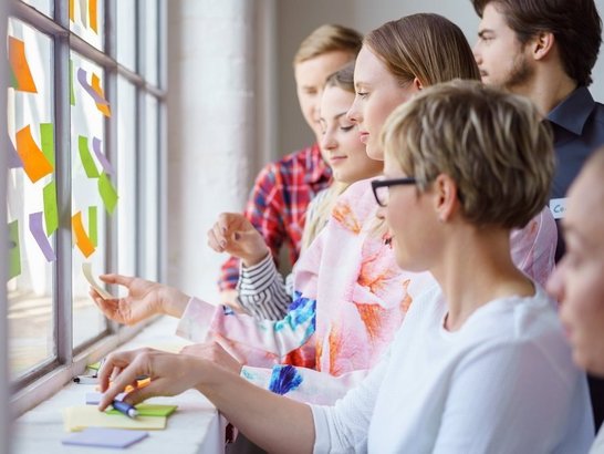 Gruppe von Personen klebt bunte Post-it in ein Glasfenster