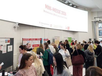 Eine gut besuchte Messehalle, auf der großen Leinwand steht "MINI-Messe 2026"
