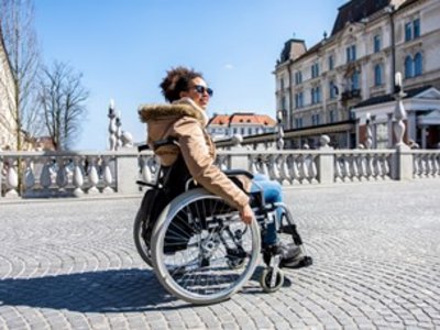 Junge Frau fährt mit Rollstuhl über eine Brücke