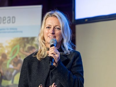 Frau spricht in Mikrofon im Hintergrund ist ein Roll-Up zu sehen