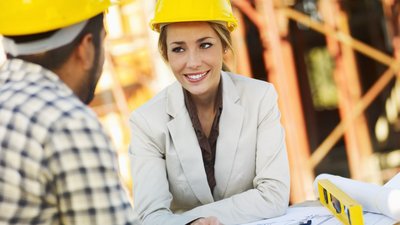 Frau und Mann mit Bauhelmen auf einer Baustelle