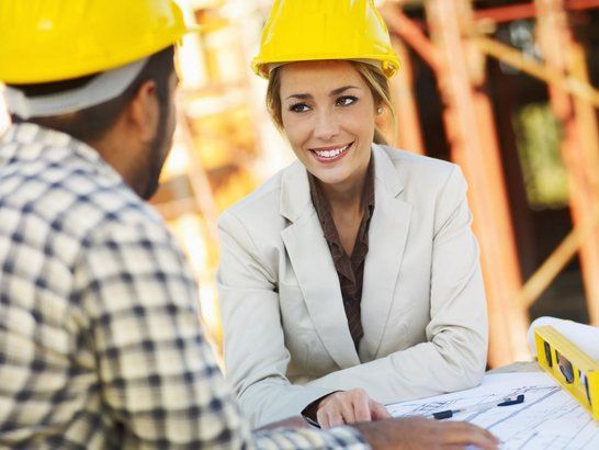 Frau und Mann mit Bauhelmen auf einer Baustelle