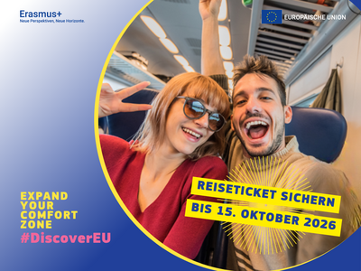 Zwei Leute sitzen im Zug und lachen in die Kamera 