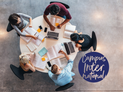 Eine Gruppe junger Menschen sitzt rund um einen runden Tisch und arbeitet gemeinsam am Laptop