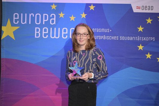 Eine Dame steht mit Pokal vor einem Transparent mit der Aufschrift "Europa bewegt" und lächelt in die Kamera
