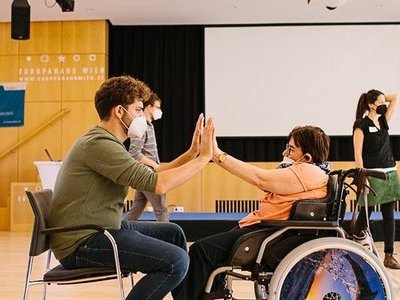 Zwei Personen im Rollstuhl geben sich die Hand