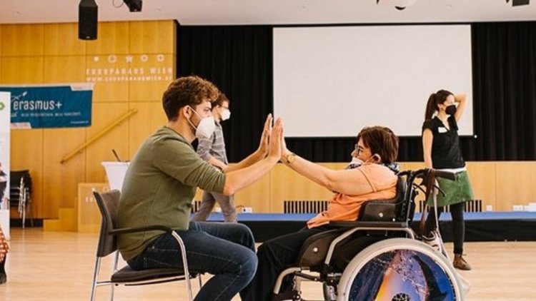 Zwei Personen im Rollstuhl geben sich die Hand 