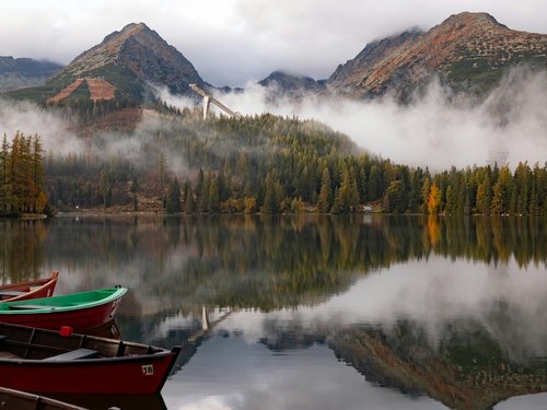 Ruhiger Bergsee mit Booten im nebligen Herbst