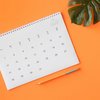 Kalender liegt auf orangener Unterlage, daneben sieht man ein Monstera Blatt