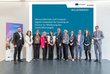 Alle Speaker der Veranstaltung stehen in einer Reihe nebeneinander auf der Bühne vor der Titelbildfolie der Präsentation. 