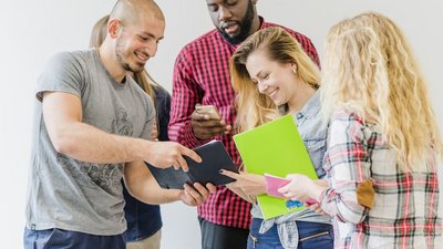 Kleine Gruppe steht im Gespräch miteinander und blicken gemeinsam auf Notizbuch