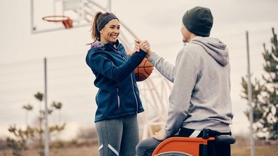 Männlcicher Sportler mit Behinderung und junge Frau beglückwünschen sich auf einem Basketballplatz im Freien