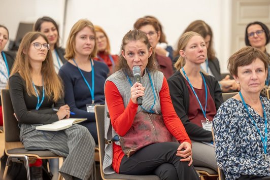 Ein Blick ins Publikum, die zentrale Person am Bild hält ein Mikrofon in der Hand und stellt gerade eine Frage.