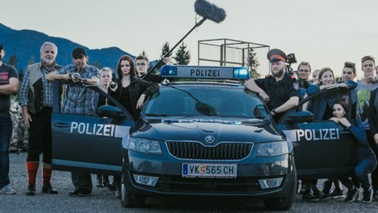 Jugendliche und Erwachsene (beim Dreh eines Spielfilmes) stehen um ein Polizei Auto versammelt
