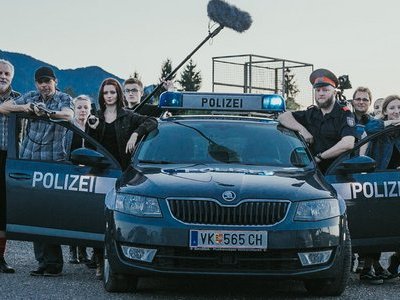 Jugendliche und Erwachsene (beim Dreh eines Spielfilmes) stehen um ein Polizei Auto versammelt