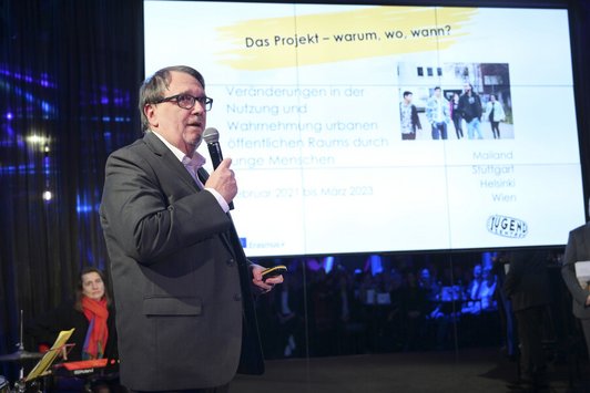 Mann hält Mikro und steht auf einer Bühne