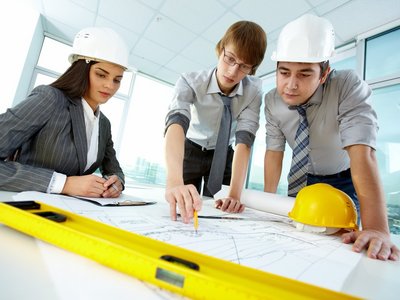 A woman and two men wearing construction site hats discuss a construction plan.