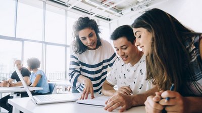 Drei junge Studierende lehnen sich gemeinsam über Notizen