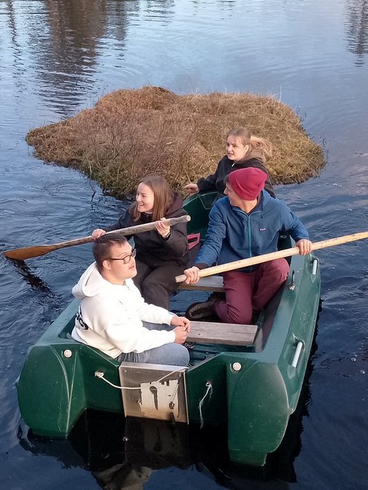 Grünes Schlauchboot auf Wasser mit vier Personen an Bord. Zwei davon halten ein Ruder in der Hand.