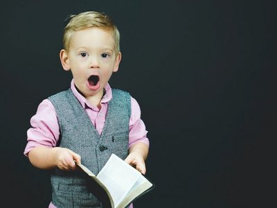 EIn blinder junge im Kindergartenalter hält ein aufgeschlagenes Buch in der Hand, ist erstaunt und hat den Mund weit offen.