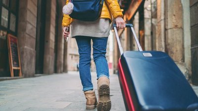 Person von hinten geht durch eine Straße und zieht ihren Rollkoffer hinter sich her