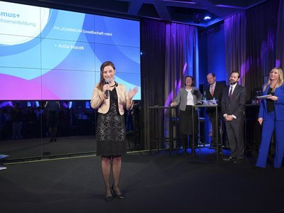 Frau steht auf der Bühne und spricht in ein Mikrofon.