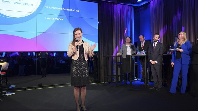 Frau steht auf der Bühne und spricht in ein Mikrofon.