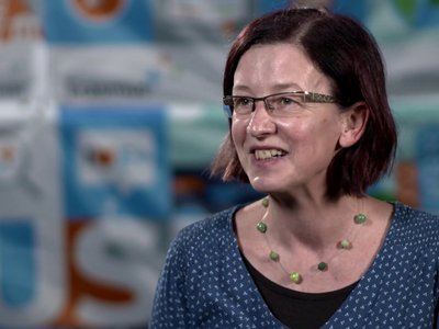 Eine Dame sitzt vor der Kamera und redet, hinter ihr steht "Erasmus+" geschrieben