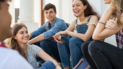 Gruppe junger Schüler/innen sitzen zusammen und unterhalten sich lachend