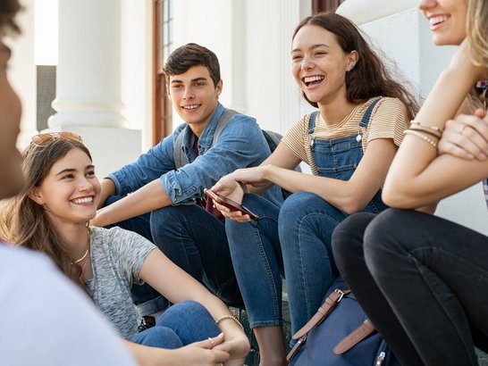 Gruppe junger Schüler/innen sitzen zusammen und unterhalten sich lachend