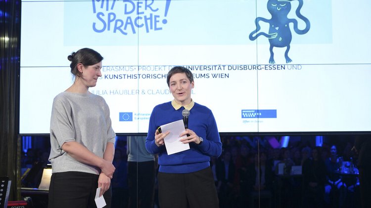 Zwei Frauen stehen auf einer Bühne und präsentieren
