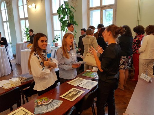 Teilnehmer/innen der Veranstaltung stehen an einem Tisch einander gegenüber und tauschen sich untereinander aus